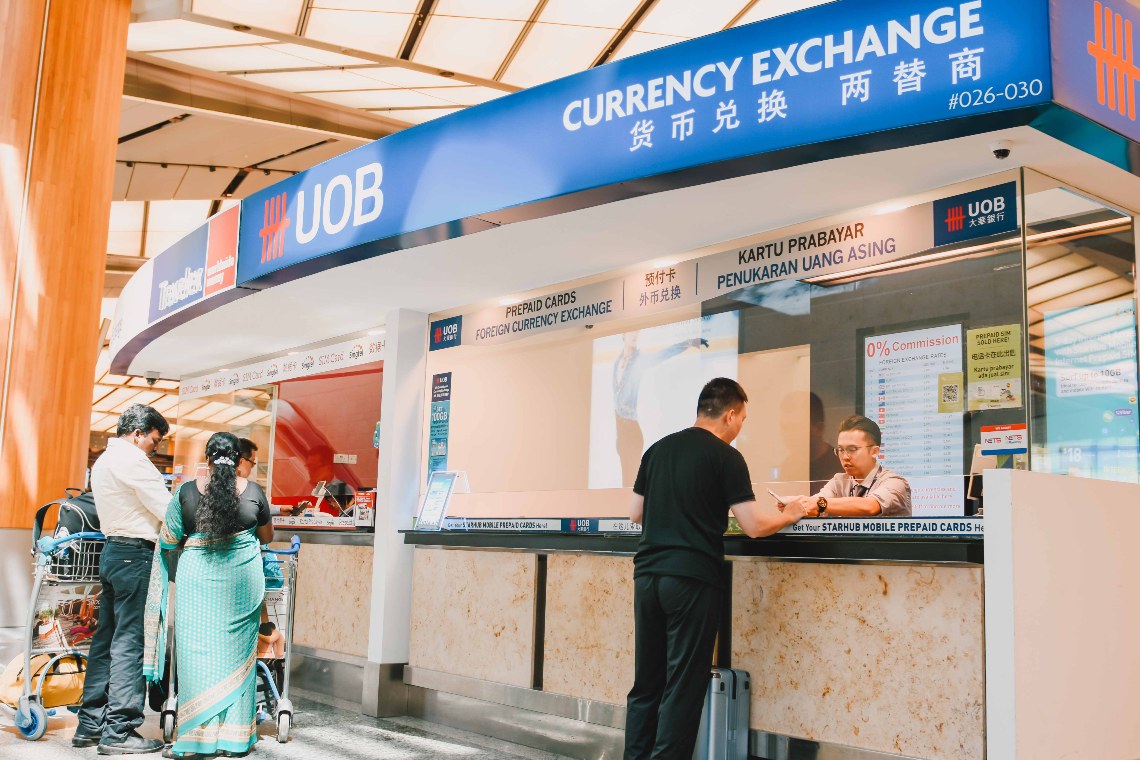 A group gathers around a currency exchange counter at the Airport